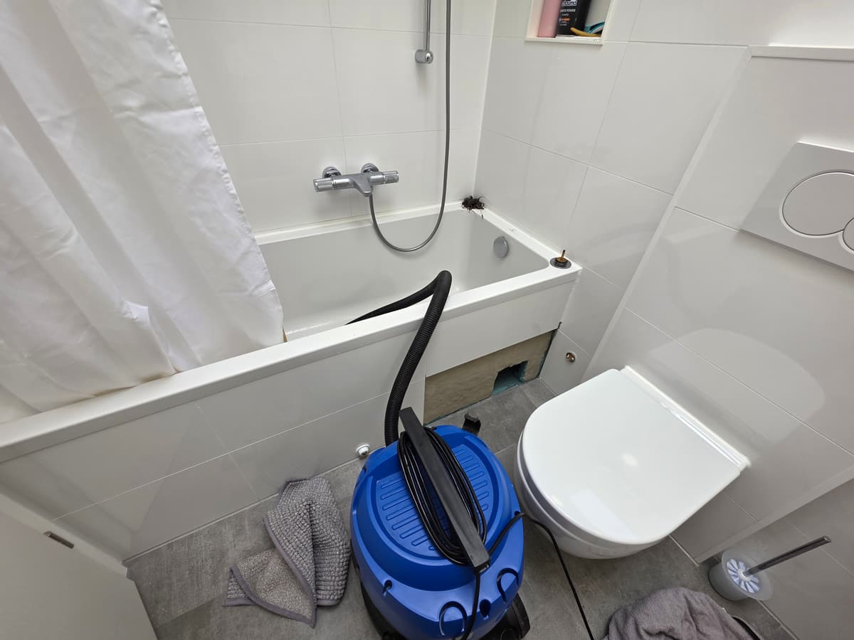 Badewanne mit geöffneter Verkleidung, davor ein Sauger, auf dem Wannenrand ein herausgezogenes Haarknäuel