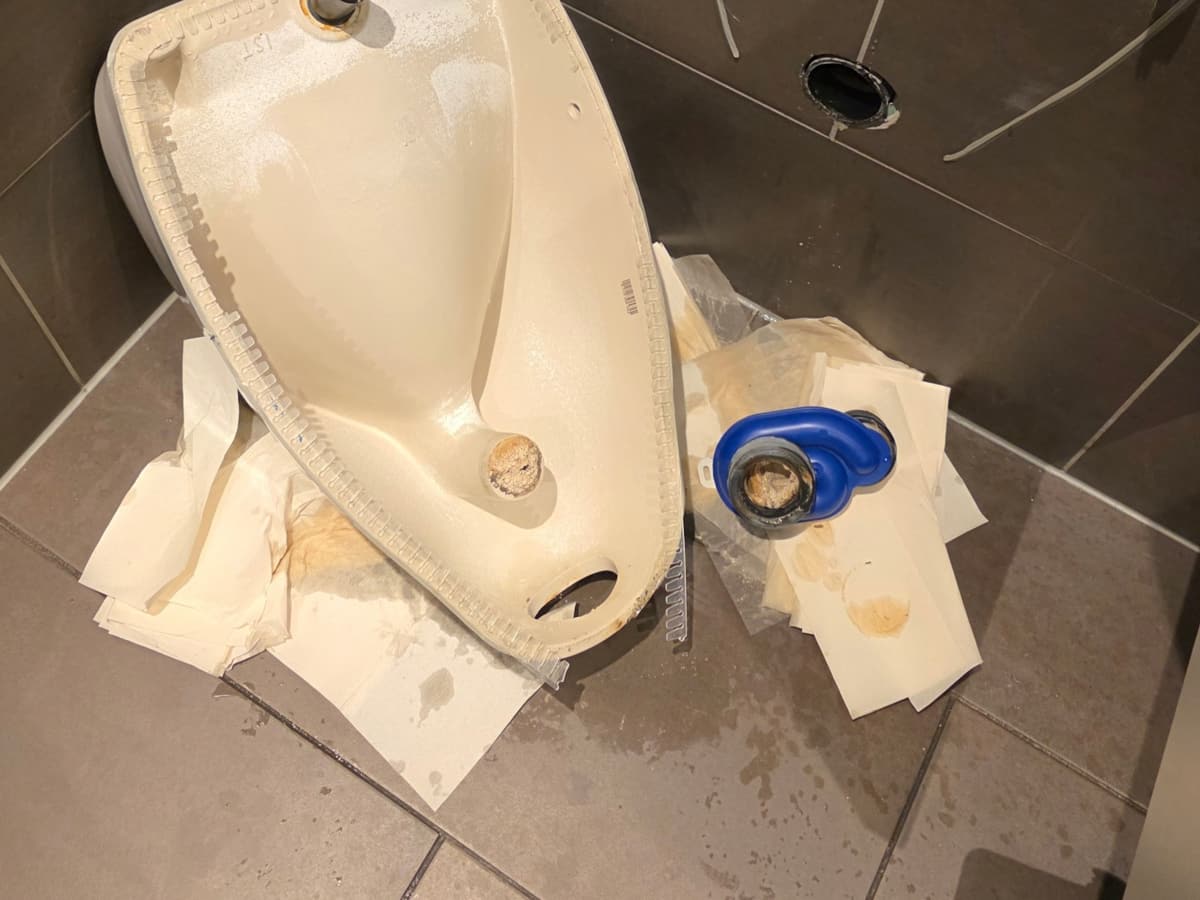 Abgenommenes Urinal mit Siphon auf dem Fliesenboden