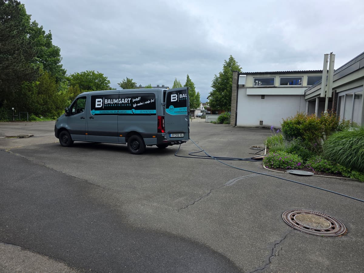 Servicefahrzeug von Rohrreinigung Baumgart im Einsatz, der Schlauch führt zum Gebäude